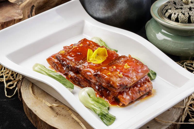 长方形瓷盘装的红烧带鱼段摆放在樟木砧板上图片