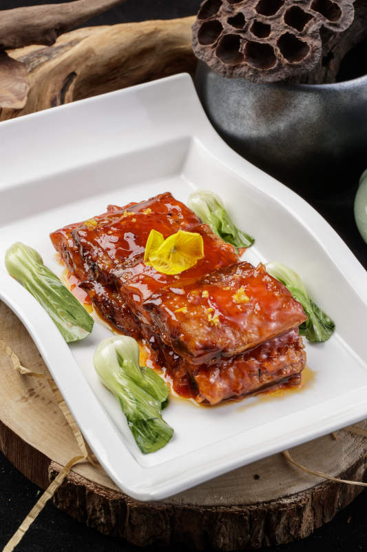 长方形瓷盘装的红烧带鱼段摆放在樟木砧板上图片