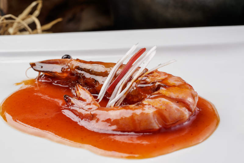 方形瓷盘装的浇汁大明虾摆放在樟木砧板上图片