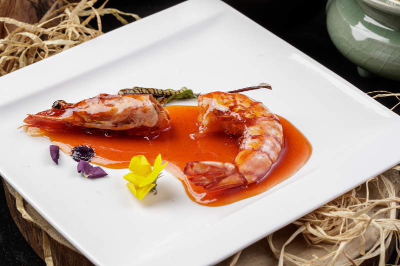 方形瓷盘装的浇汁大明虾摆放在樟木砧板上图片