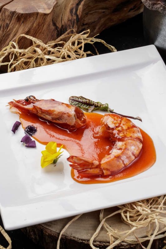 方形瓷盘装的浇汁大明虾摆放在樟木砧板上图片