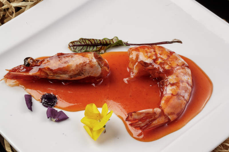 方形瓷盘装的浇汁大明虾摆放在樟木砧板上图片