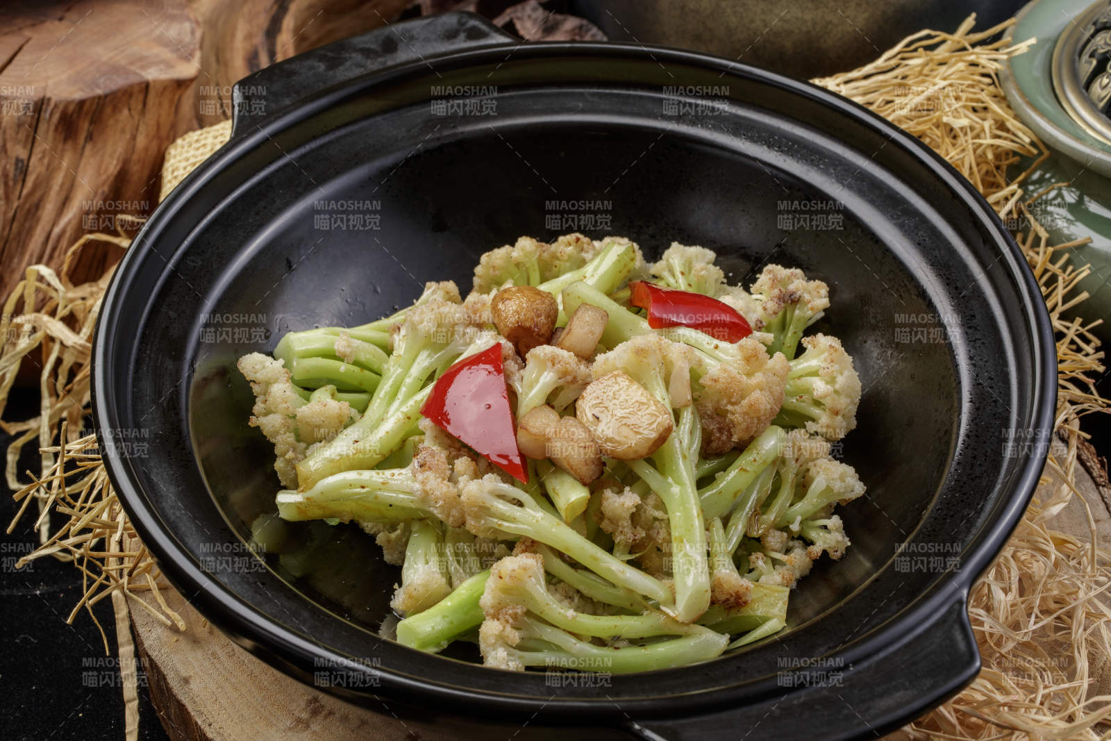 黑色砂锅装的蒜香有机菜花摆放在樟木砧板上图片