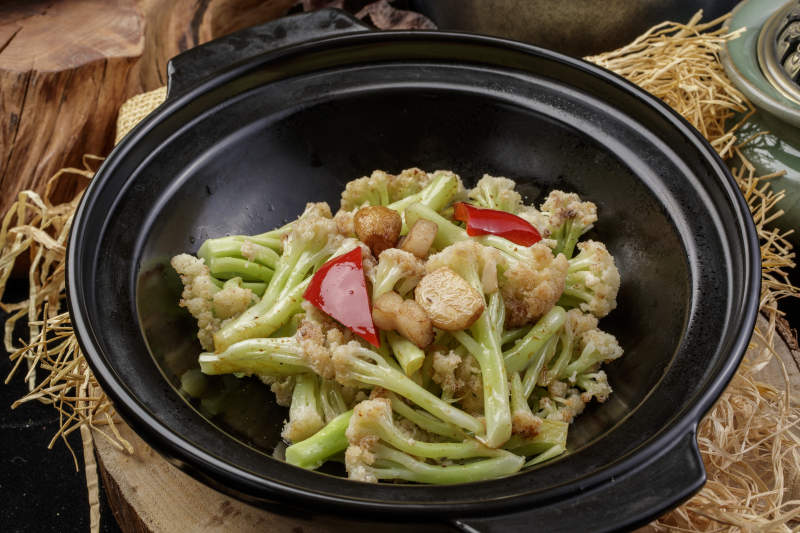 黑色砂锅装的蒜香有机菜花摆放在樟木砧板上图片