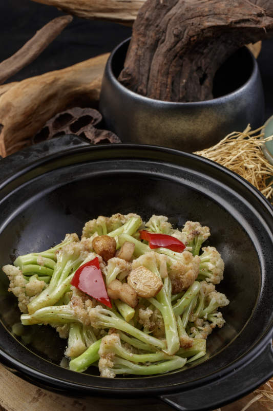 黑色砂锅装的蒜香有机菜花摆放在樟木砧板上图片