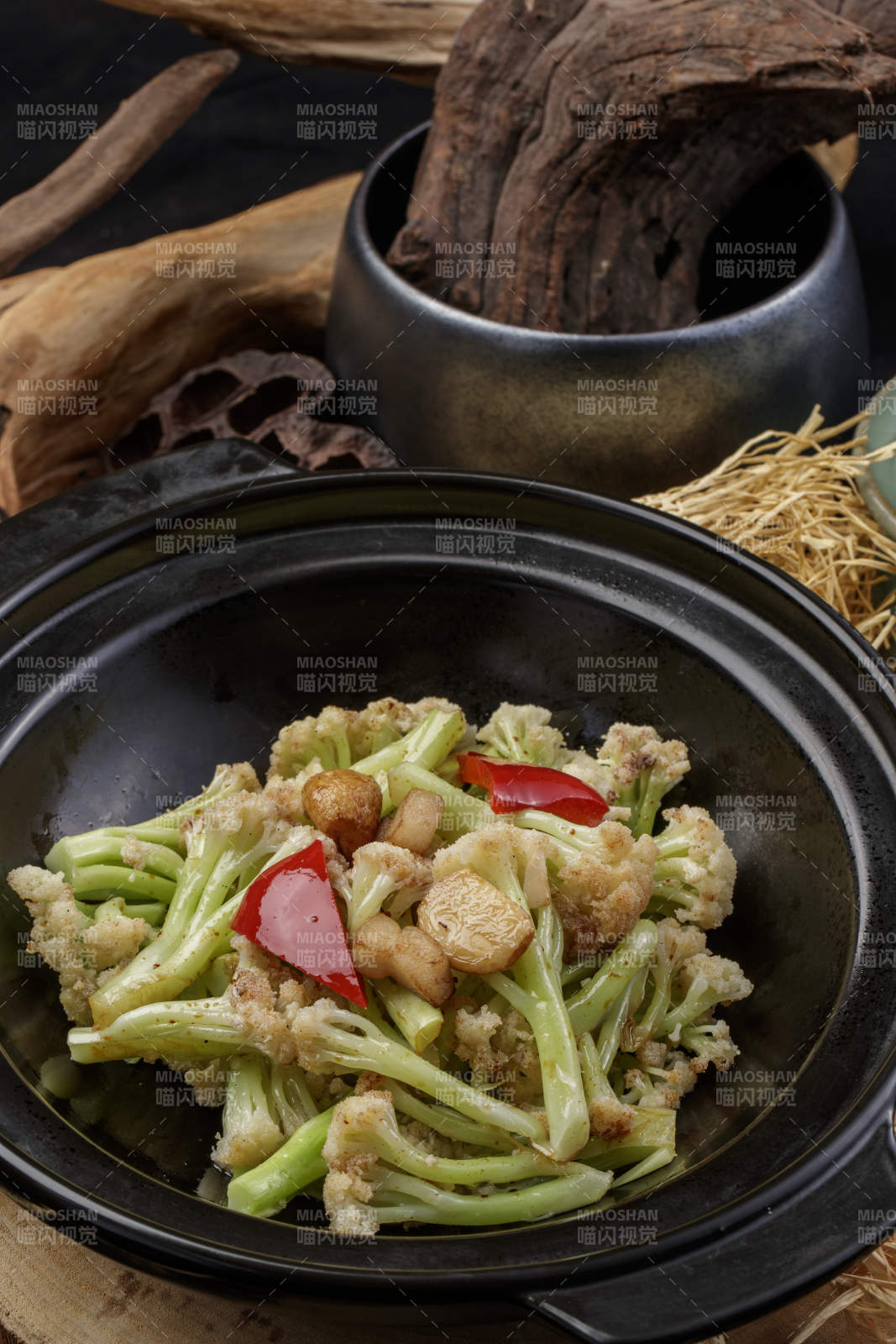 黑色砂锅装的蒜香有机菜花摆放在樟木砧板上图片