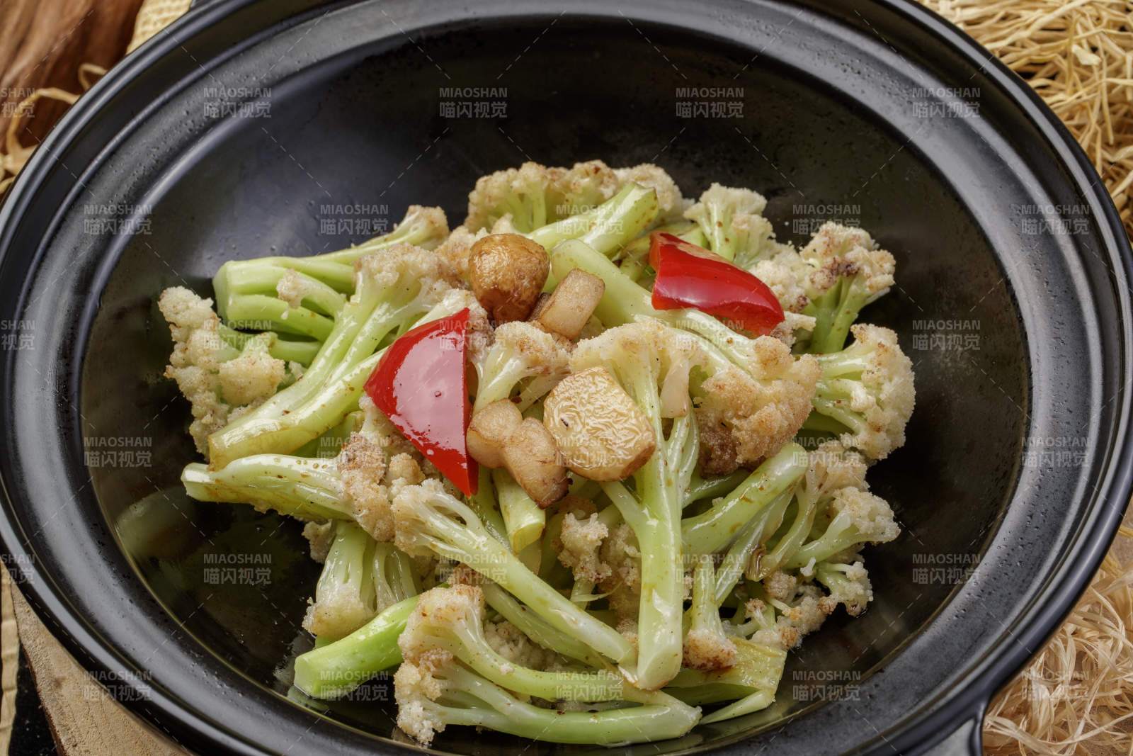 黑色砂锅装的蒜香有机菜花摆放在樟木砧板上图片