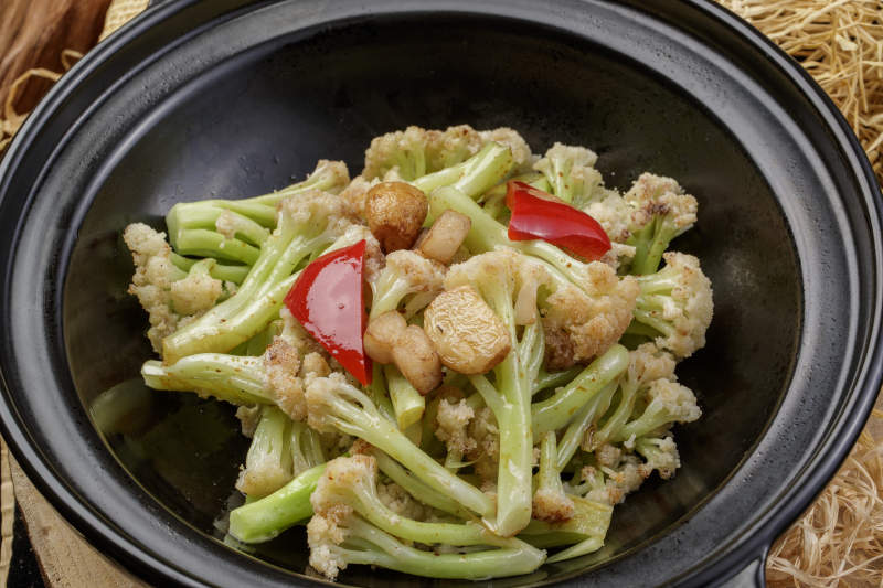 黑色砂锅装的蒜香有机菜花摆放在樟木砧板上图片