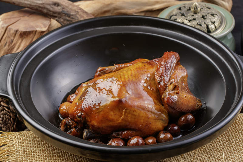 黑色砂锅装的板栗鸡摆放在麻布垫子上图片