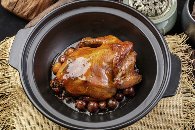 黑色砂锅装的板栗鸡摆放在麻布垫子上图片