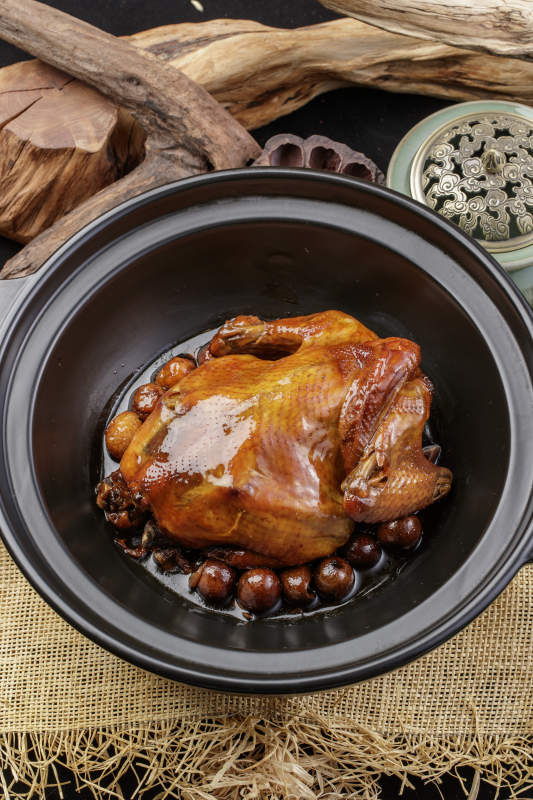 黑色砂锅装的板栗鸡摆放在麻布垫子上图片