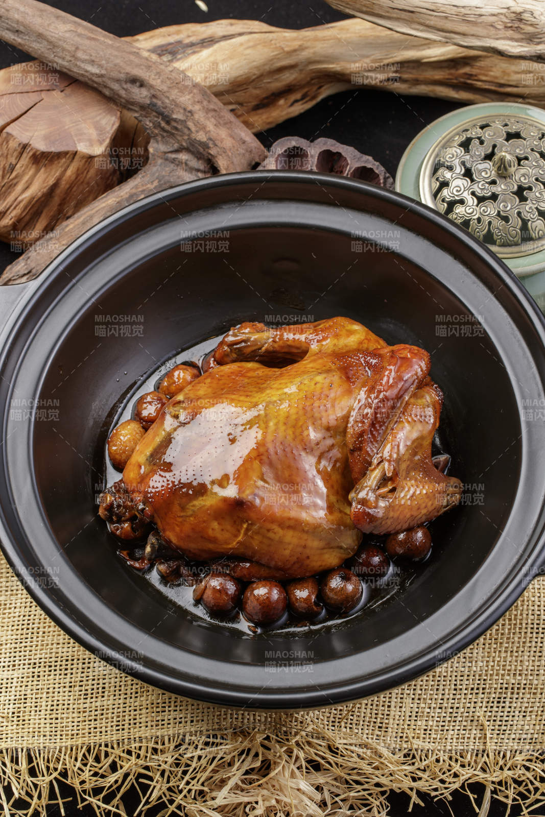 黑色砂锅装的板栗鸡摆放在麻布垫子上图片