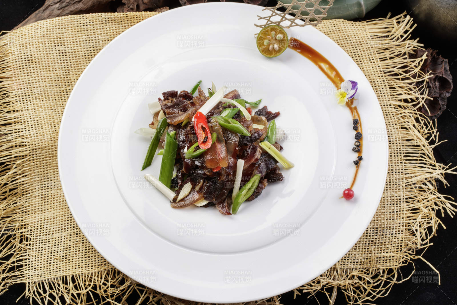 圆形瓷盘装的杭椒蒜薹炒黑腊肉摆放在麻布垫子上图片