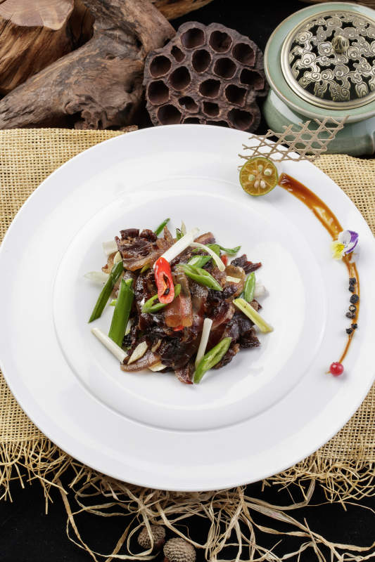 圆形瓷盘装的杭椒蒜薹炒黑腊肉摆放在麻布垫子上图片