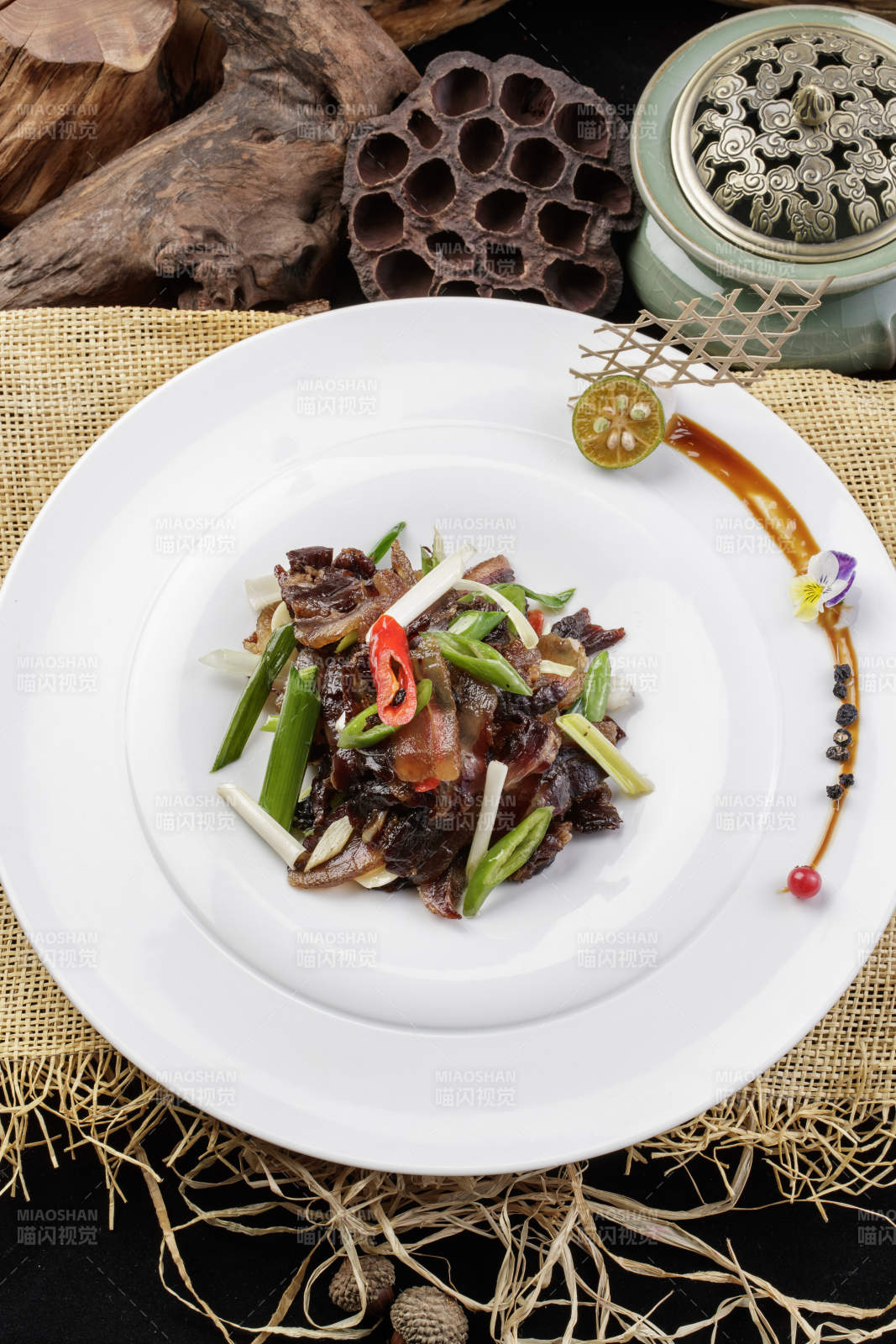 圆形瓷盘装的杭椒蒜薹炒黑腊肉摆放在麻布垫子上图片