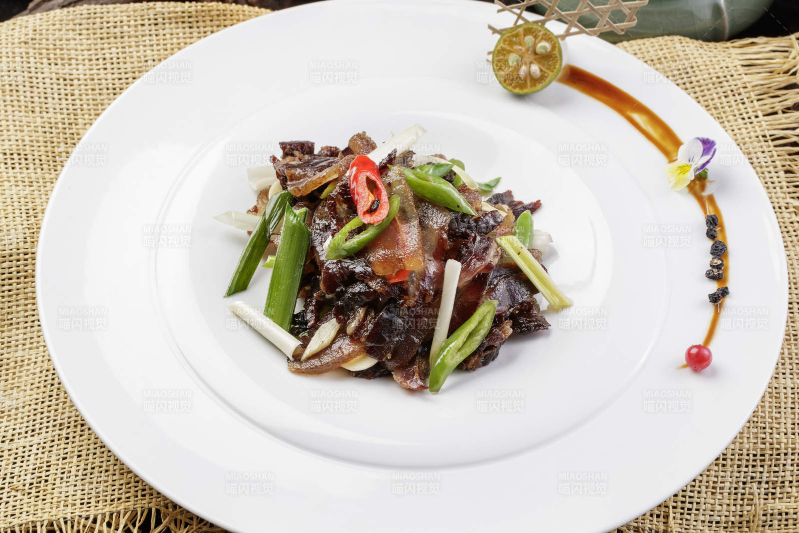 圆形瓷盘装的杭椒蒜薹炒黑腊肉摆放在麻布垫子上图片