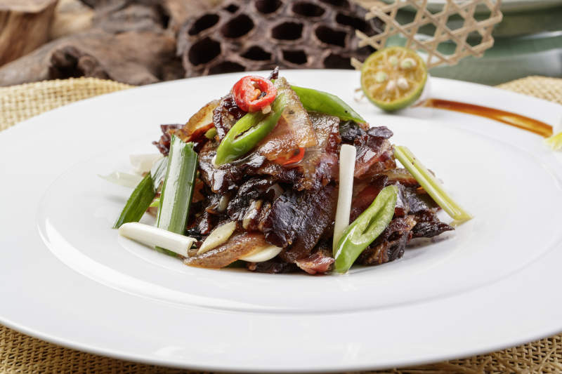 圆形瓷盘装的杭椒蒜薹炒黑腊肉摆放在麻布垫子上图片