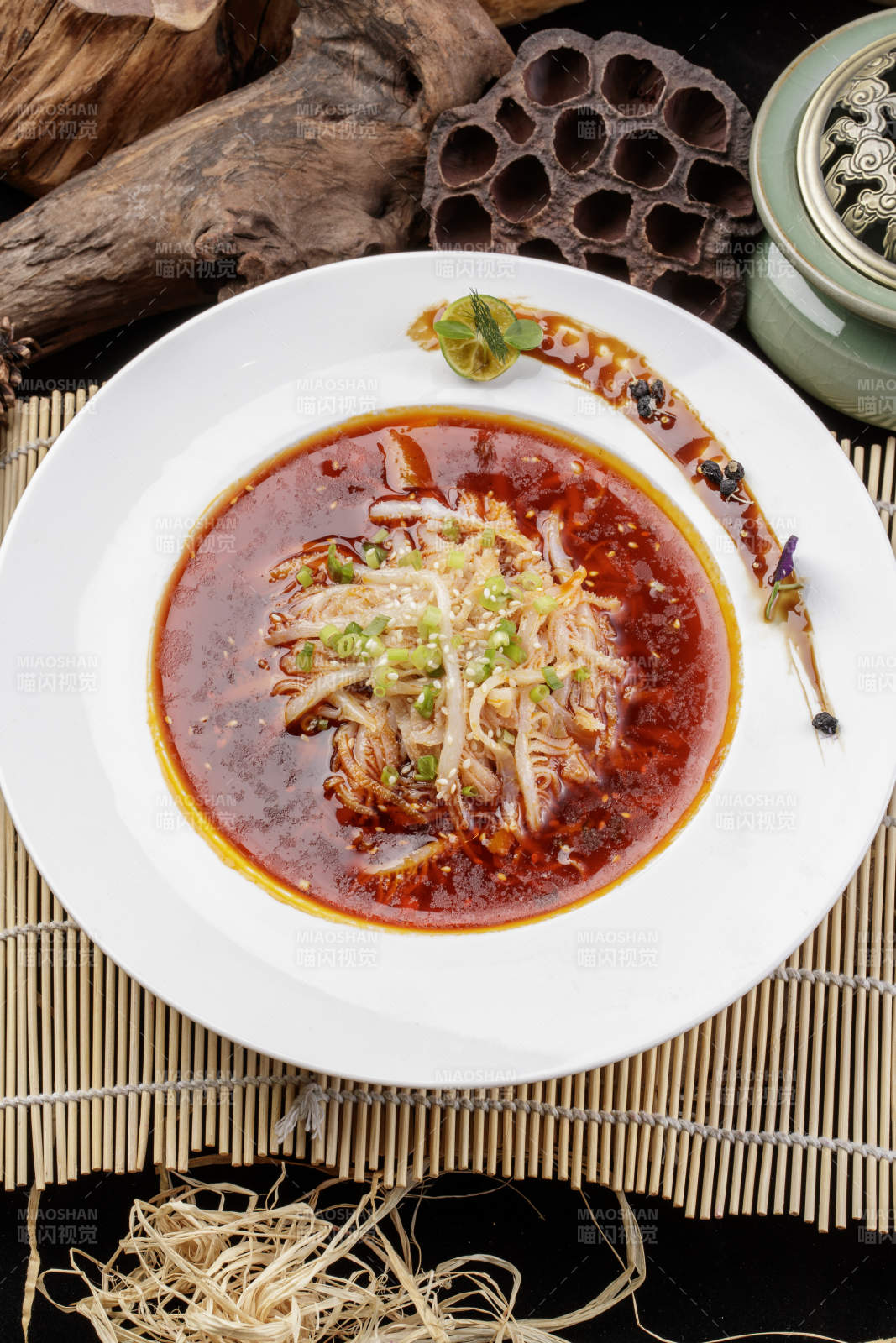 圆形瓷盘装的红油肚丝摆放在寿司帘上图片