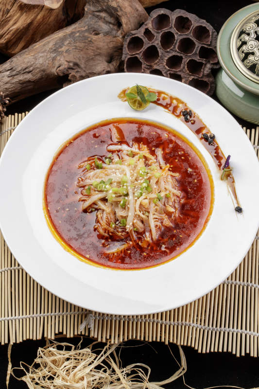 圆形瓷盘装的红油肚丝摆放在寿司帘上图片