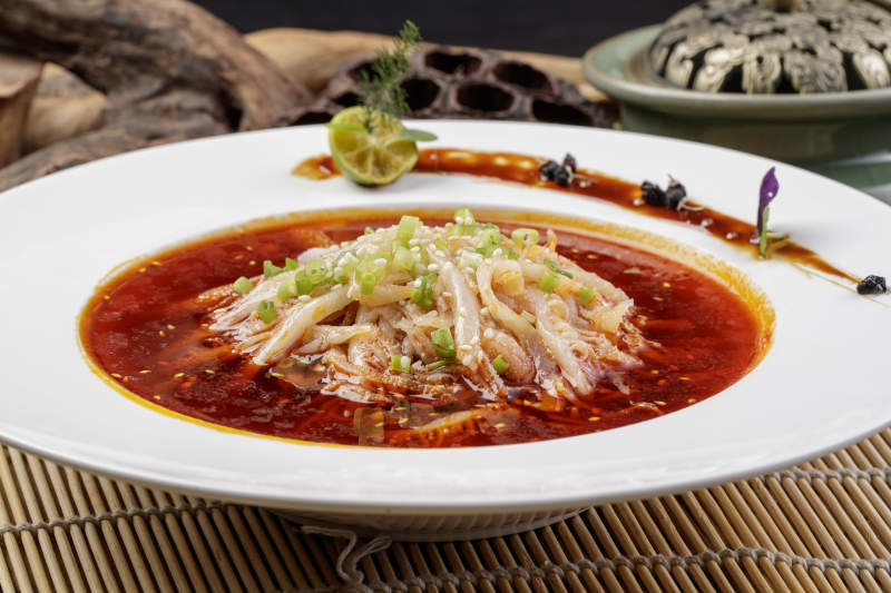 圆形瓷盘装的红油肚丝摆放在寿司帘上图片