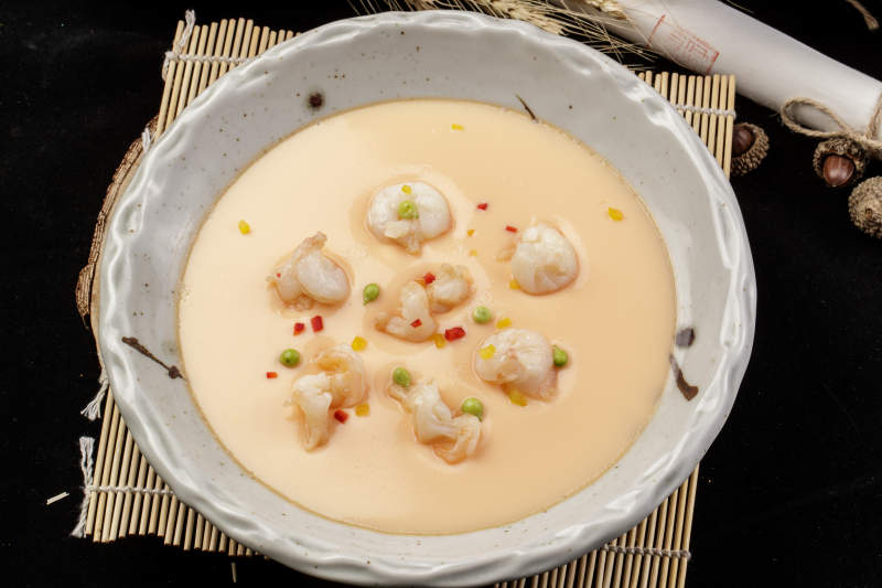 米色圆盘装的虾仁蒸水蛋摆放在寿司帘上图片