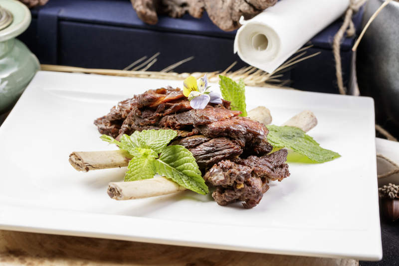 方形瓷盘装的脱骨酱牛肋摆放在樟木砧板上图片