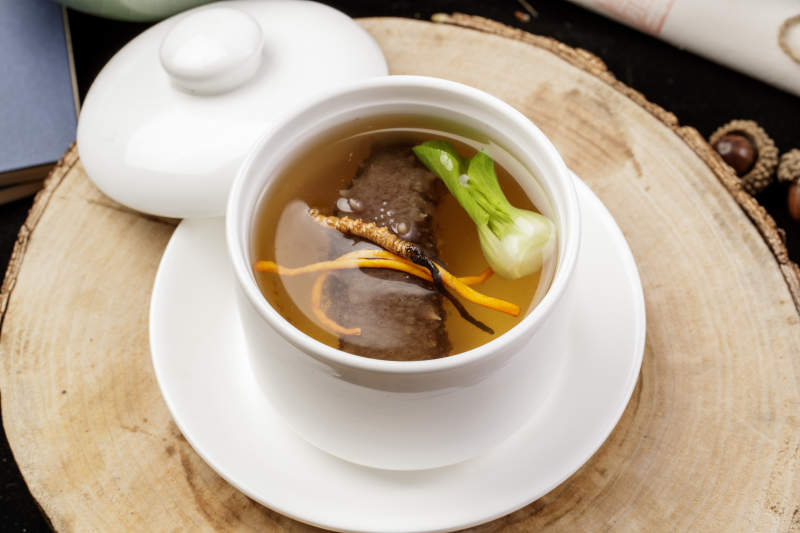 滋补虫草花海参汤摆放在樟木砧板上图片