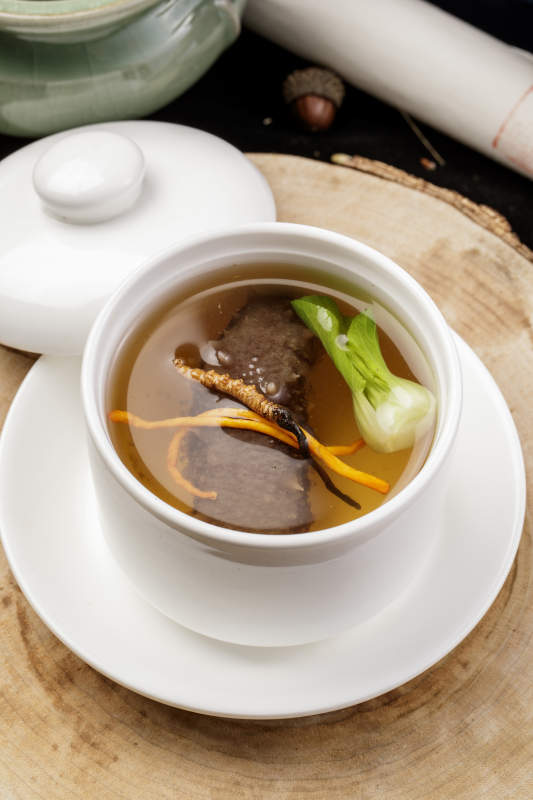 滋补虫草花海参汤摆放在樟木砧板上图片