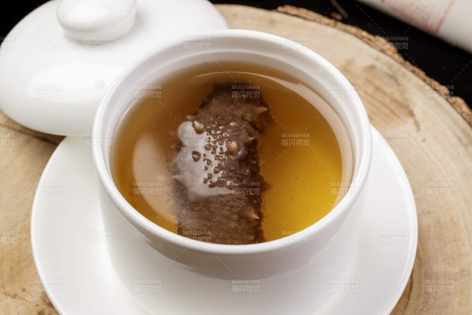 白色汤盅装的海参汤摆放在樟木砧板上图片