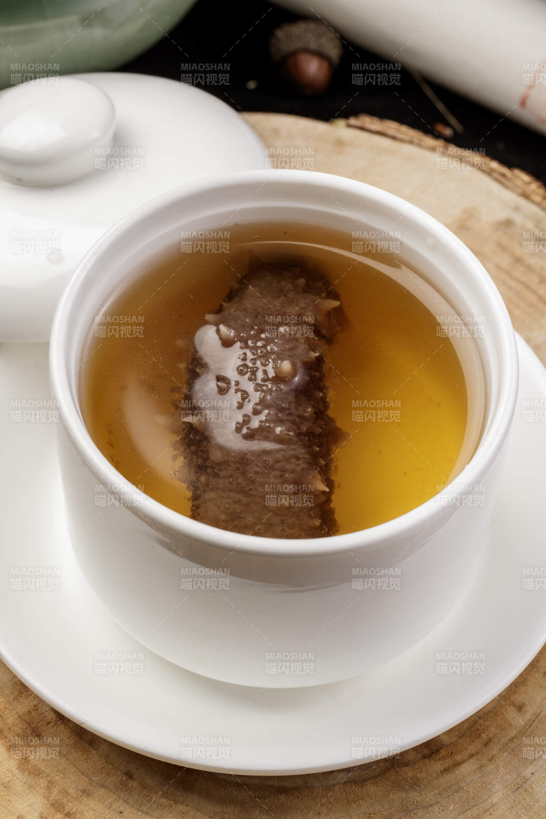 白色汤盅装的海参汤摆放在樟木砧板上图片