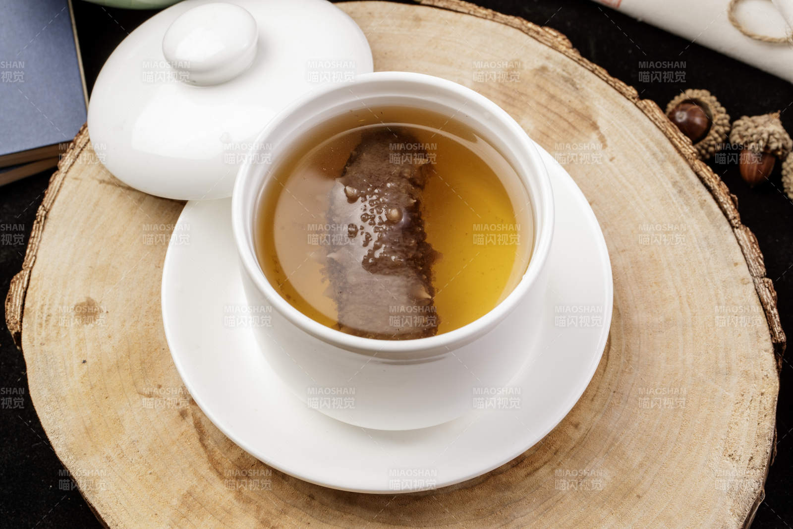 白色汤盅装的海参汤摆放在樟木砧板上图片