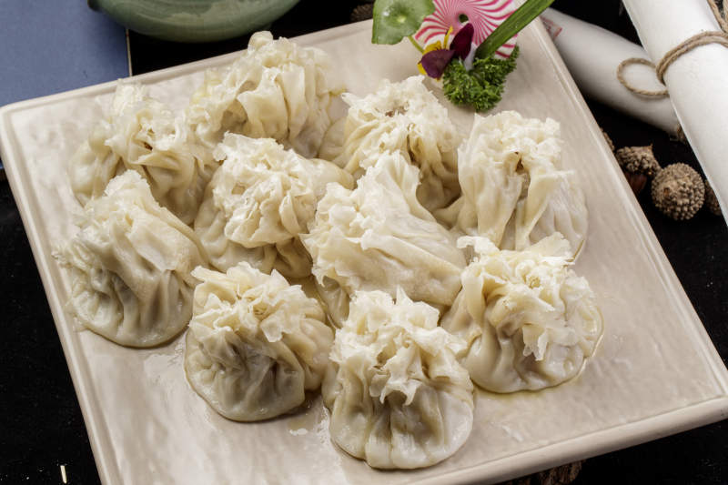 米色瓷盘装的美味烧麦摆放在黑色背景上图片