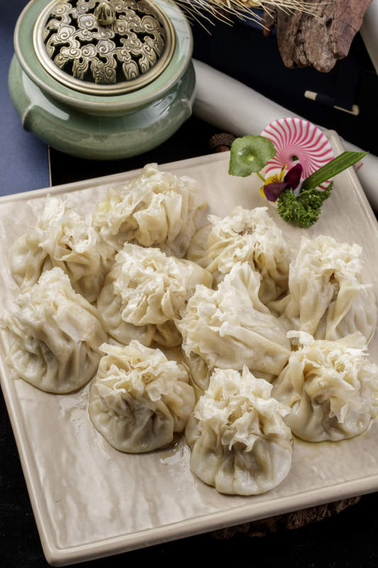 米色瓷盘装的美味烧麦摆放在黑色背景上图片