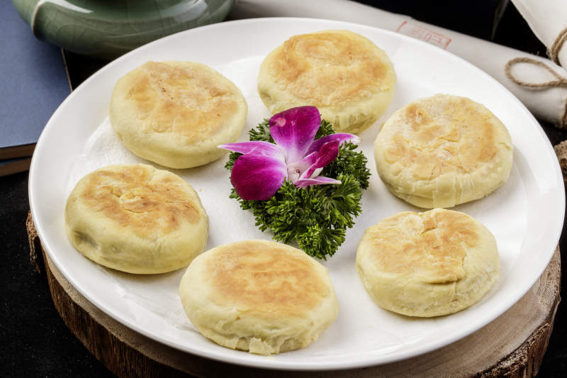 圆形瓷盘装的咸鱼酥饼摆放在樟木砧板上图片