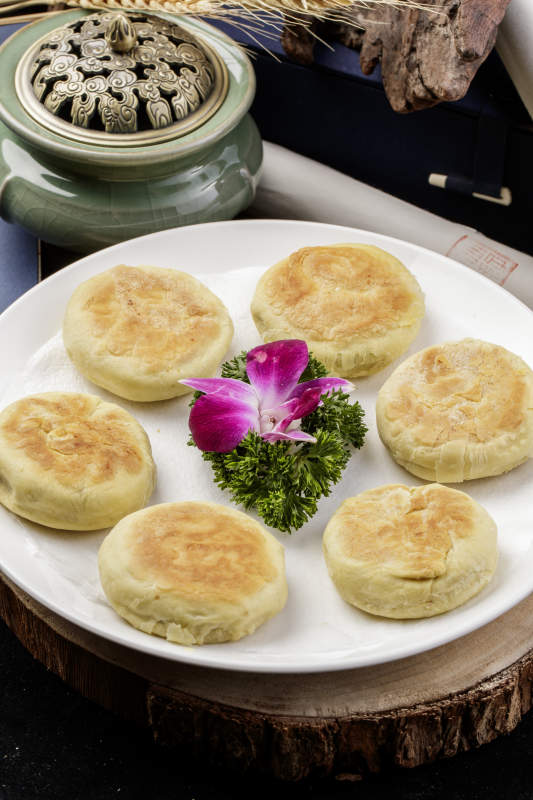 圆形瓷盘装的咸鱼酥饼摆放在樟木砧板上图片