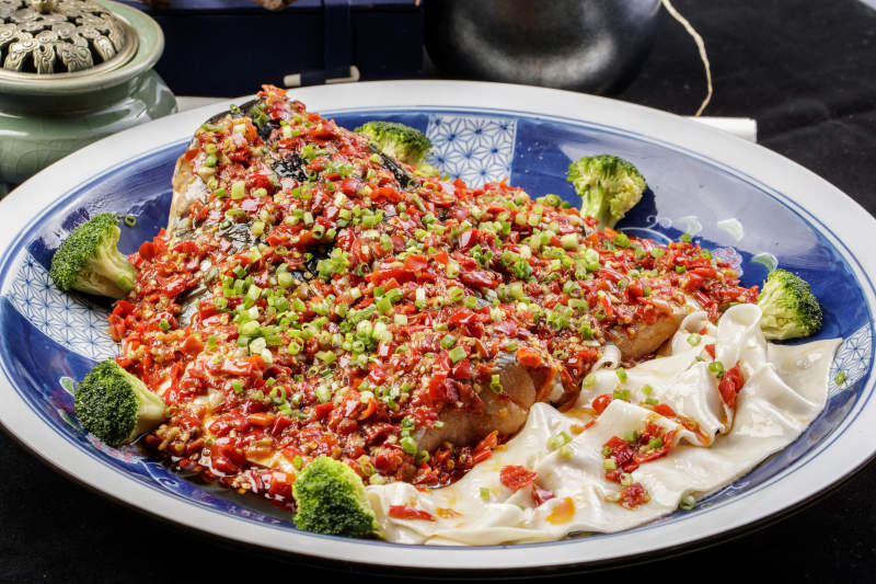 青花瓷盘装的剁椒鱼头盖面摆放在黑色背景上图片