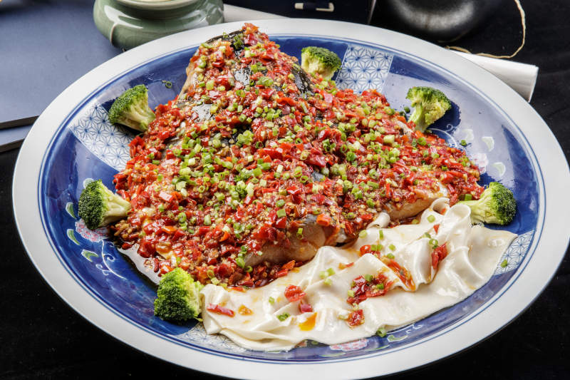 青花瓷盘装的剁椒鱼头盖面摆放在黑色背景上图片