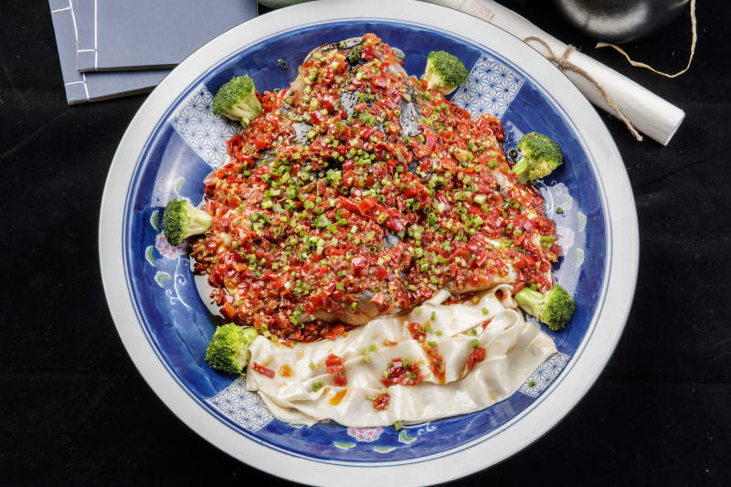 青花瓷盘装的剁椒鱼头盖面摆放在黑色背景上图片