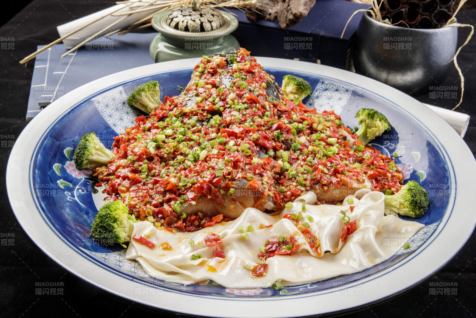 青花瓷盘装的剁椒鱼头盖面摆放在黑色背景上图片