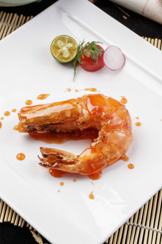 方形瓷盘装的油煎浇汁深海虾摆放在寿司帘上图片