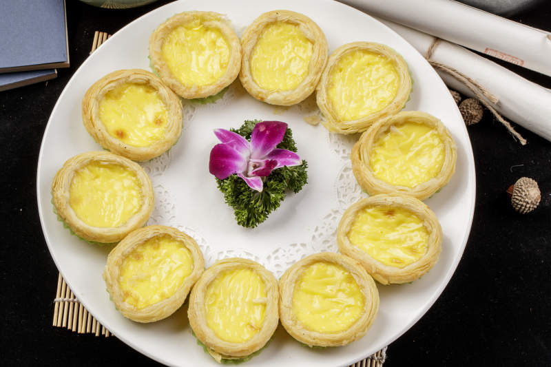 白色瓷盘装的葡式蛋挞摆放在寿司帘上图片