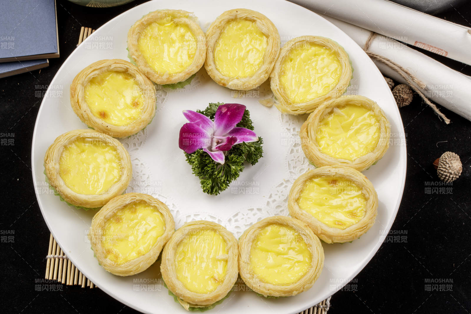 白色瓷盘装的葡式蛋挞摆放在寿司帘上图片