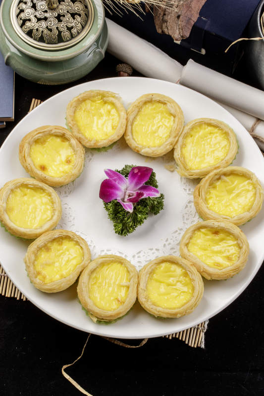 白色瓷盘装的葡式蛋挞摆放在寿司帘上图片