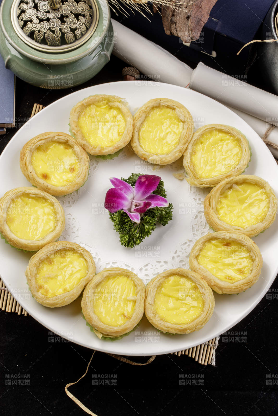 白色瓷盘装的葡式蛋挞摆放在寿司帘上图片