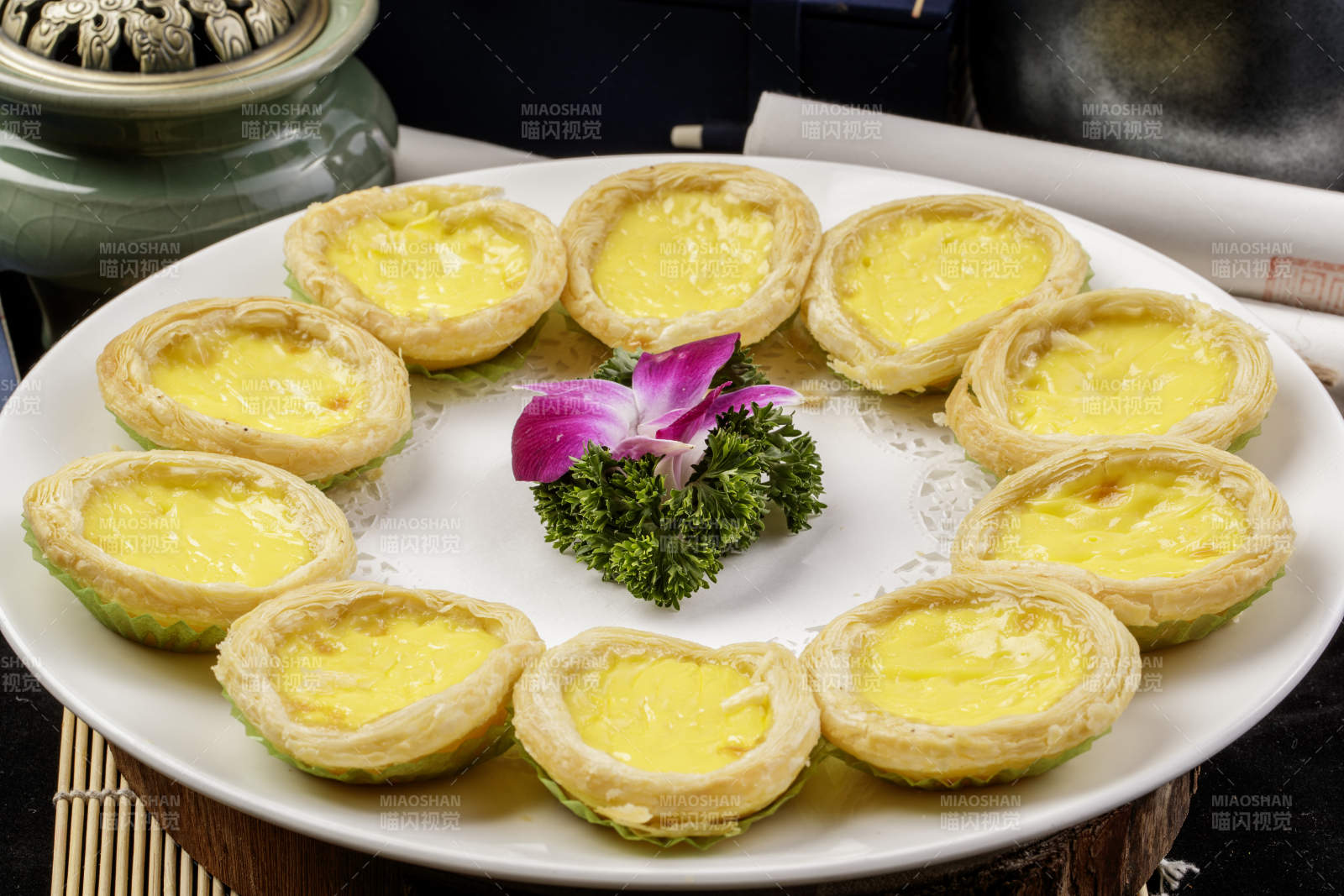 白色瓷盘装的葡式蛋挞摆放在寿司帘上图片