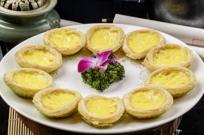 白色瓷盘装的葡式蛋挞摆放在寿司帘上图片