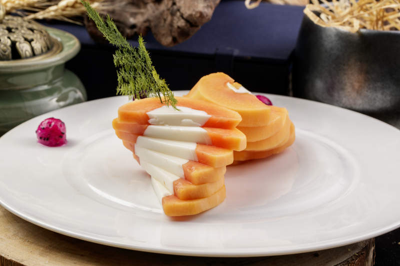 白色圆瓷盘装的木瓜蛋白摆放在樟木砧板上图片