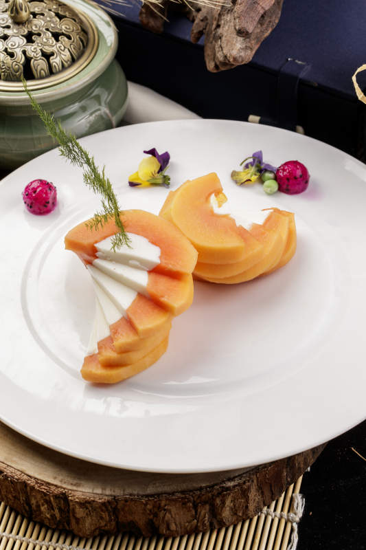 白色圆瓷盘装的木瓜蛋白摆放在樟木砧板上图片