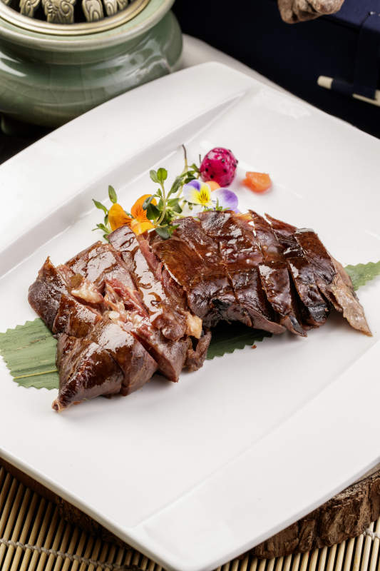 白瓷盘装的苏州酱鸭摆放在寿司帘上图片