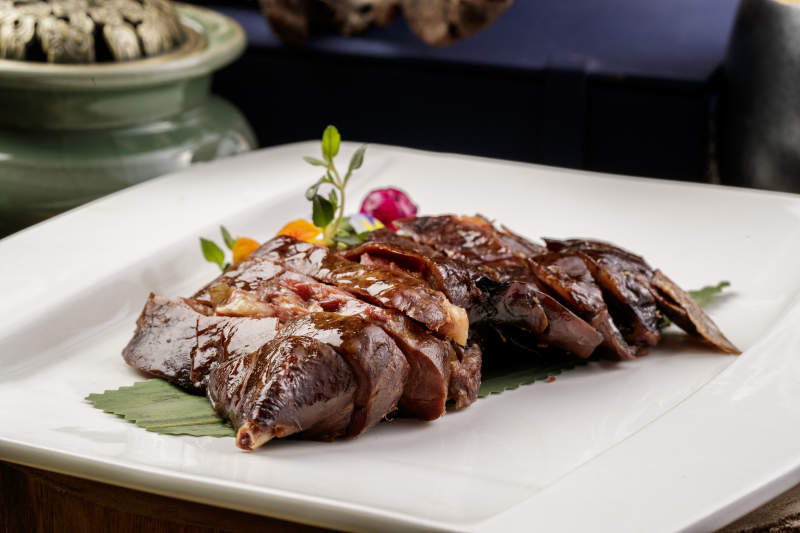 白瓷盘装的苏州酱鸭摆放在寿司帘上图片